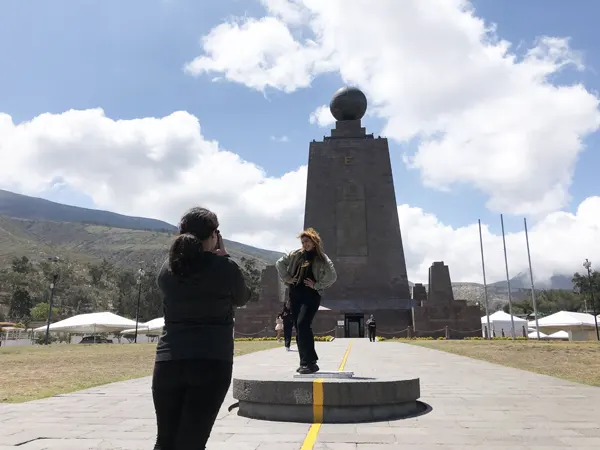 Una chica tomando una foto a otra en la Línea del Ecuador con el monumento al fondo