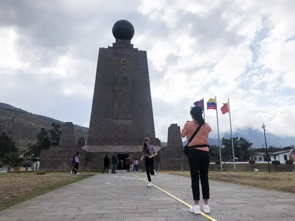 Persona saltando sobre la franja pintada que representa la linea ecuatorial frente al monumento de la mitad del mundo